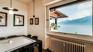 Ein Essbereich mit Tisch, Stühlen, gerahmten Bildern und Blick auf einen See und Berge durch ein großes Fenster.