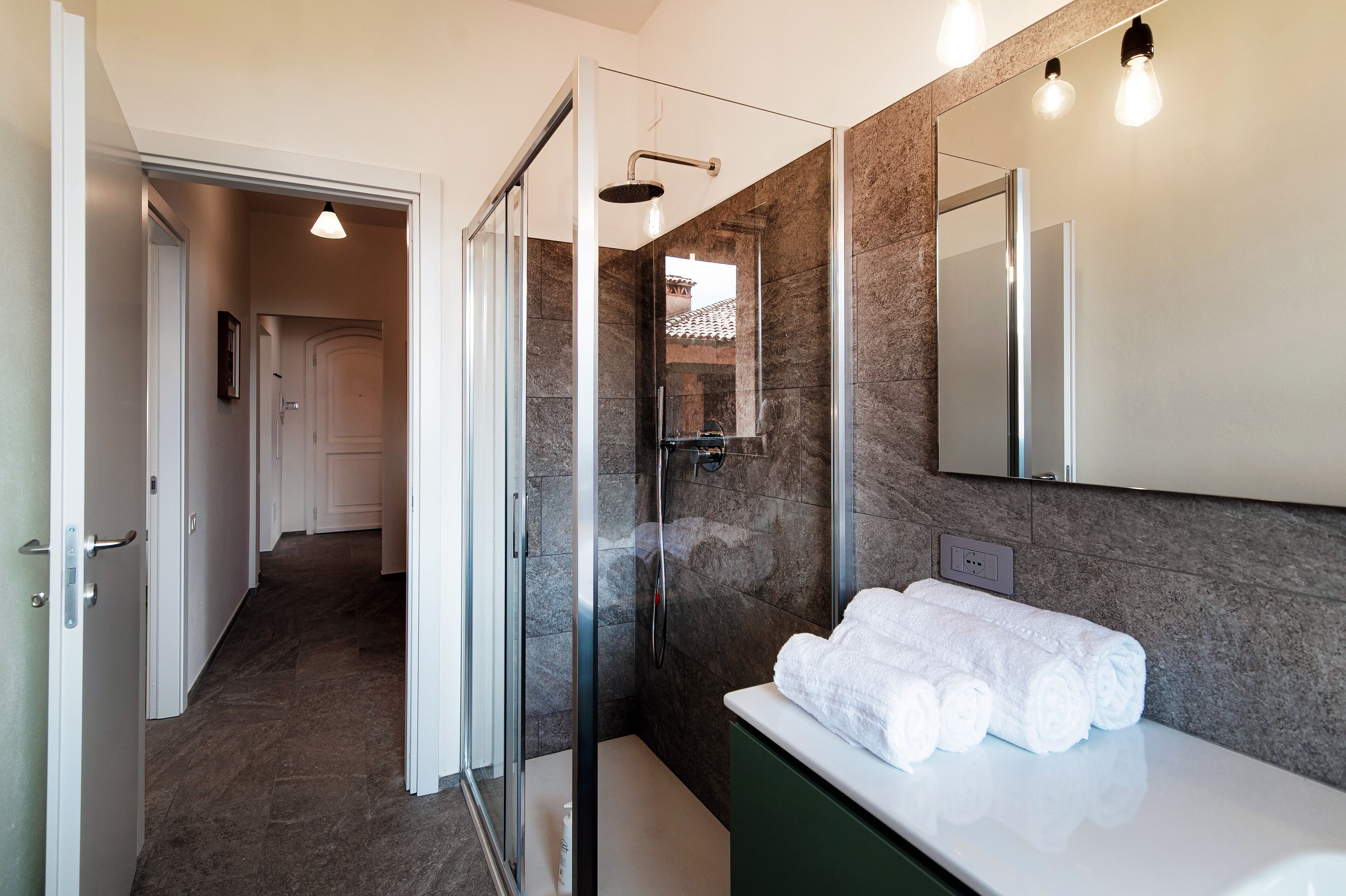 A modern bathroom with a glass-enclosed shower, a white sink with a green cabinet, and a mirror above the sink.