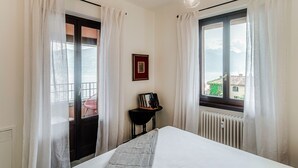 Ein Hotelzimmer mit einem Bett, einem kleinen Tisch mit Bilderrahmen, einem Stuhl und Blick auf die Stadt durch das Fenster.
