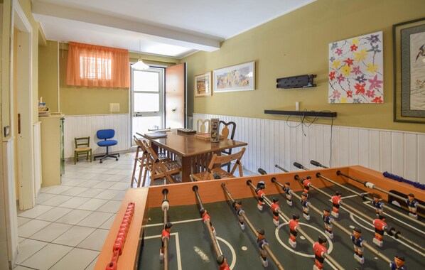 Een kamer met een tafelvoetbaltafel, een eettafel, stoelen, een blauwe bureaustoel en kunst aan de wanden.