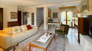 Una sala de estar con sofá, sillón, mesa de centro y televisor. Una escalera conduce a otra habitación.