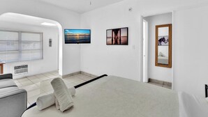 Une chambre d’hôtel moderne dotée d’un grand lit, d’un coin salon avec un fauteuil et une petite table, d’une grande fenêtre avec des stores et d’œuvres d’art accrochées aux murs.