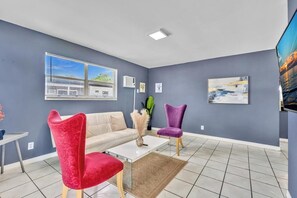 Een moderne woonkamer met een bank, twee stoelen, een salontafel en kunstwerken aan de wanden.