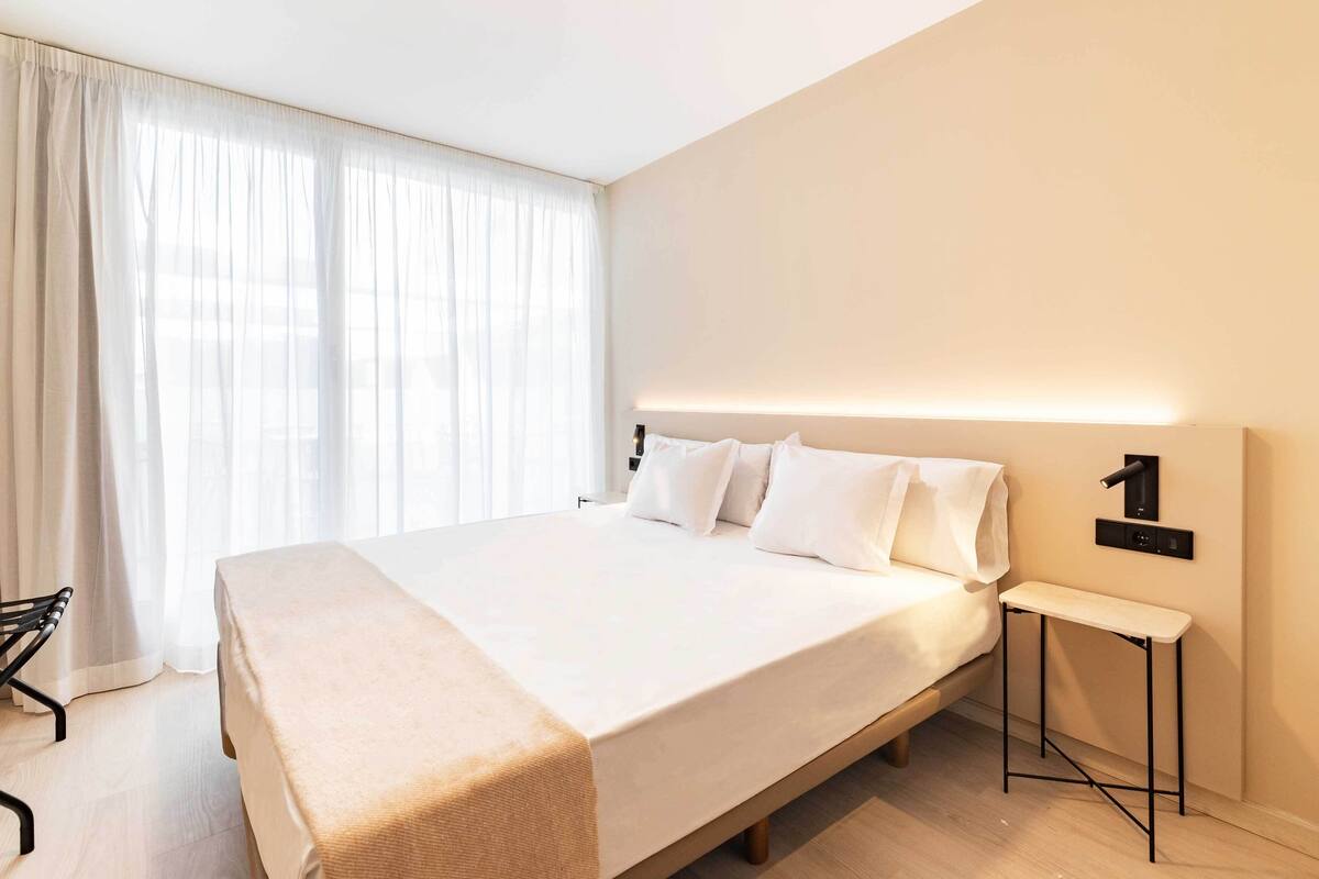 A modern hotel room with a large bed, a bedside table, and a wall-mounted light fixture.
