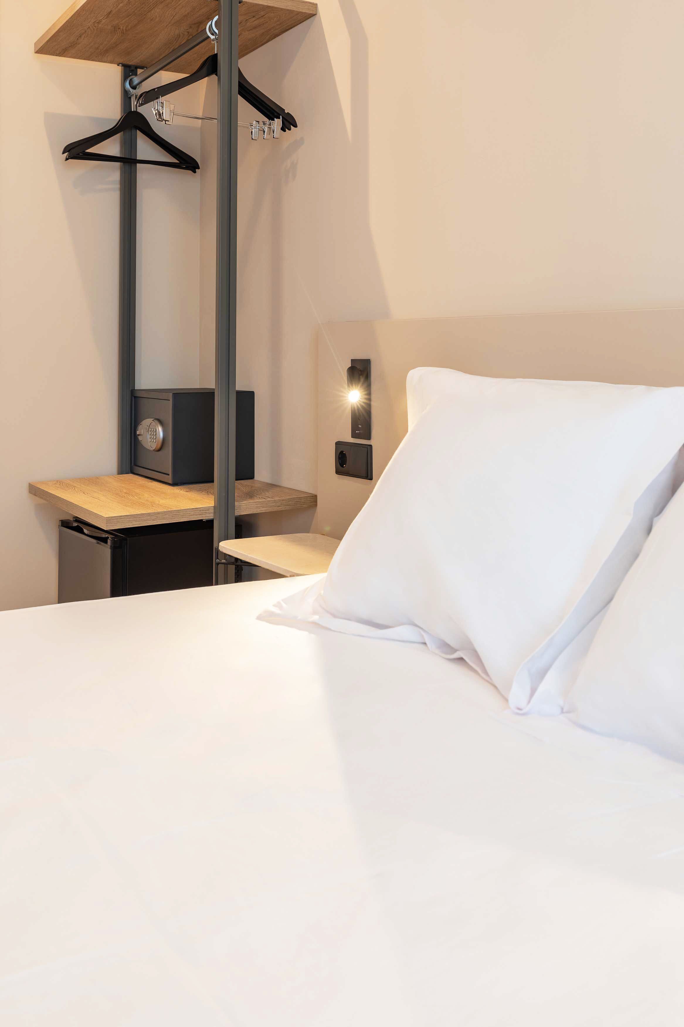 A hotel room with a bed, a desk with a computer, a coat rack, and a safe.