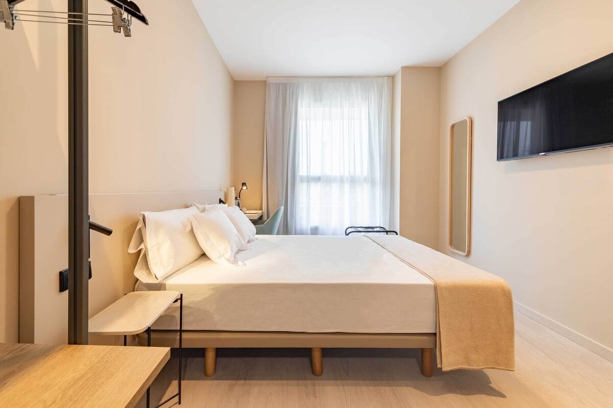 A modern hotel room with a bed, bedside table, and a TV mounted on the wall.