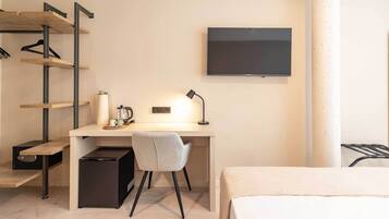 Una habitación de hotel compacta con escritorio, silla, cama, televisor y una kitchenette pequeña.
