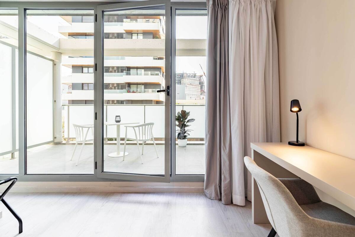 A modern apartment with a sliding glass door leading to a balcony, a small table, and a chair.