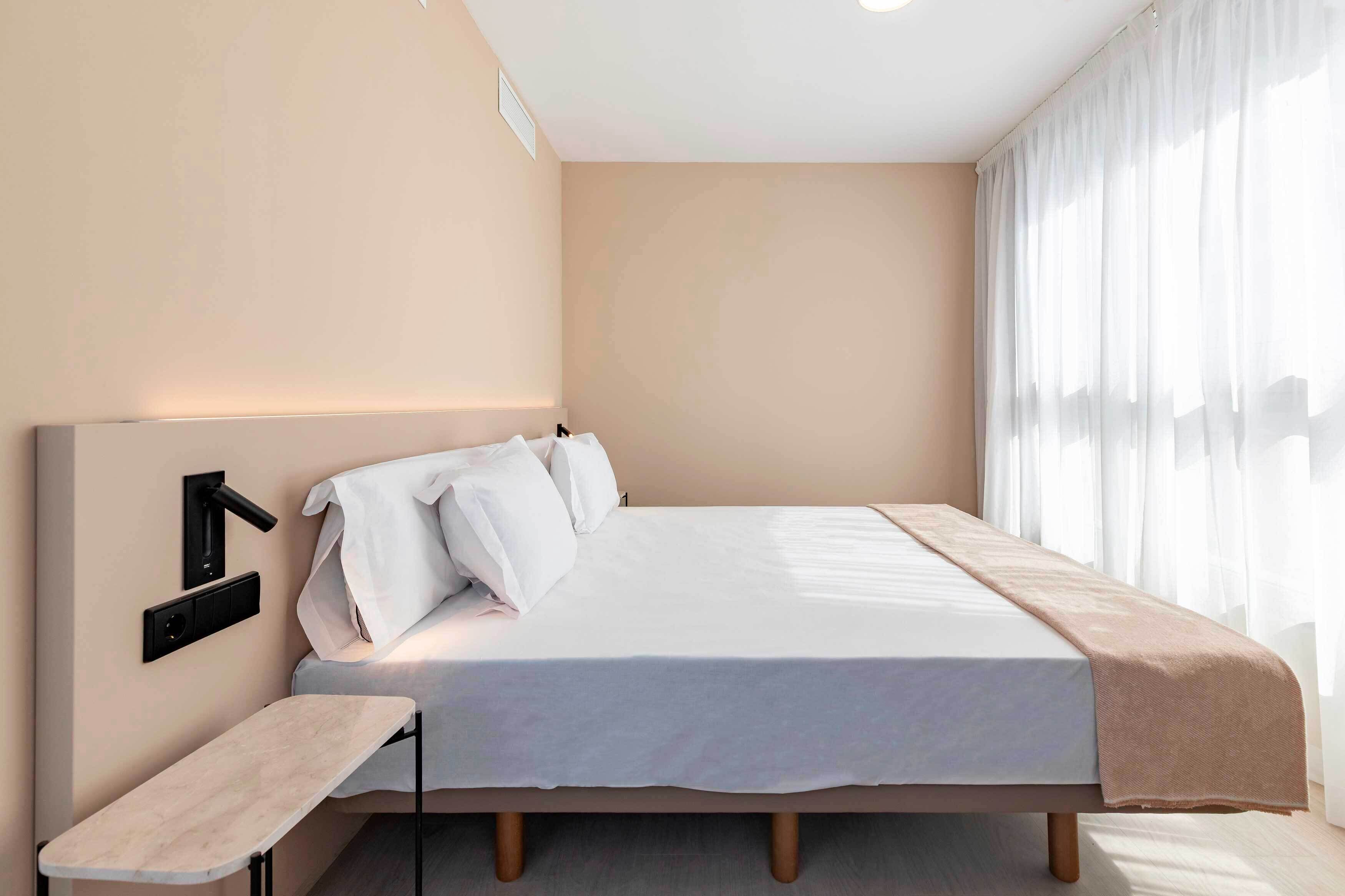 A modern bedroom with a bed, bedside table, and a wall-mounted light fixture.