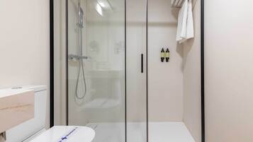Une salle de bain moderne avec une douche à parois de verre, des toilettes blanches et un porte-serviettes avec deux serviettes.