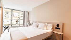 Et moderne hotelværelse med en stor seng, et lille skrivebord og udsigt over byen gennem gulv til loft-vinduer.