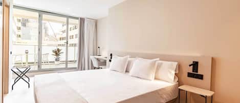 Habitación de hotel moderna con una cama grande, un escritorio pequeño y vistas de la ciudad a través de ventanas de piso a techo.