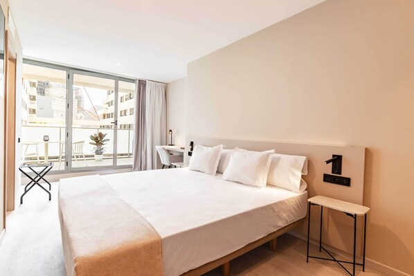 A modern hotel room with a large bed, a small desk, and a view of the city through floor-to-ceiling windows. - HQ Arena Hotel (Valencia)