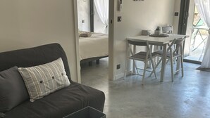 Een moderne woonkamer met een donkergrijze bank, een witte salontafel, en een eethoek met witte stoelen en een tafel.