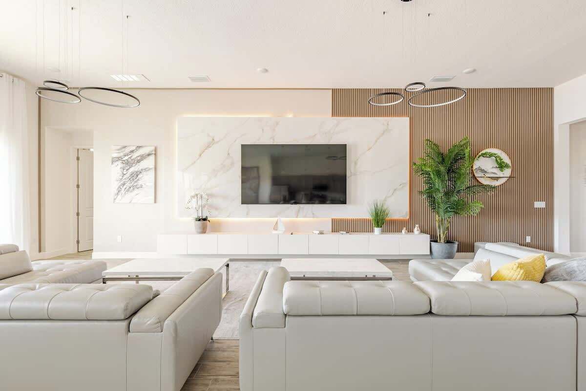 A modern living room with a large flat-screen TV, white sofas, a wooden accent wall, and a potted plant.