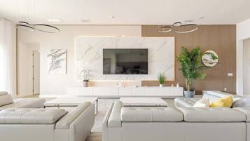 A modern living room with a large flat-screen TV, white sofas, a wooden accent wall, and a potted plant.