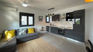 A modern kitchen with grey cabinets, a built-in oven, and a black countertop. There is a grey sofa with yellow cushions in the living area. - Superior 2-Bedroom boutique apartment with Stunning Views & Modern Amenities (Cómpeta)
