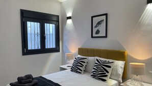 A neatly made bed with a black and white patterned pillow, a pair of folded towels, and a bedside lamp on a white nightstand. - Superior 2-Bedroom boutique apartment with Stunning Views & Modern Amenities (Cómpeta)