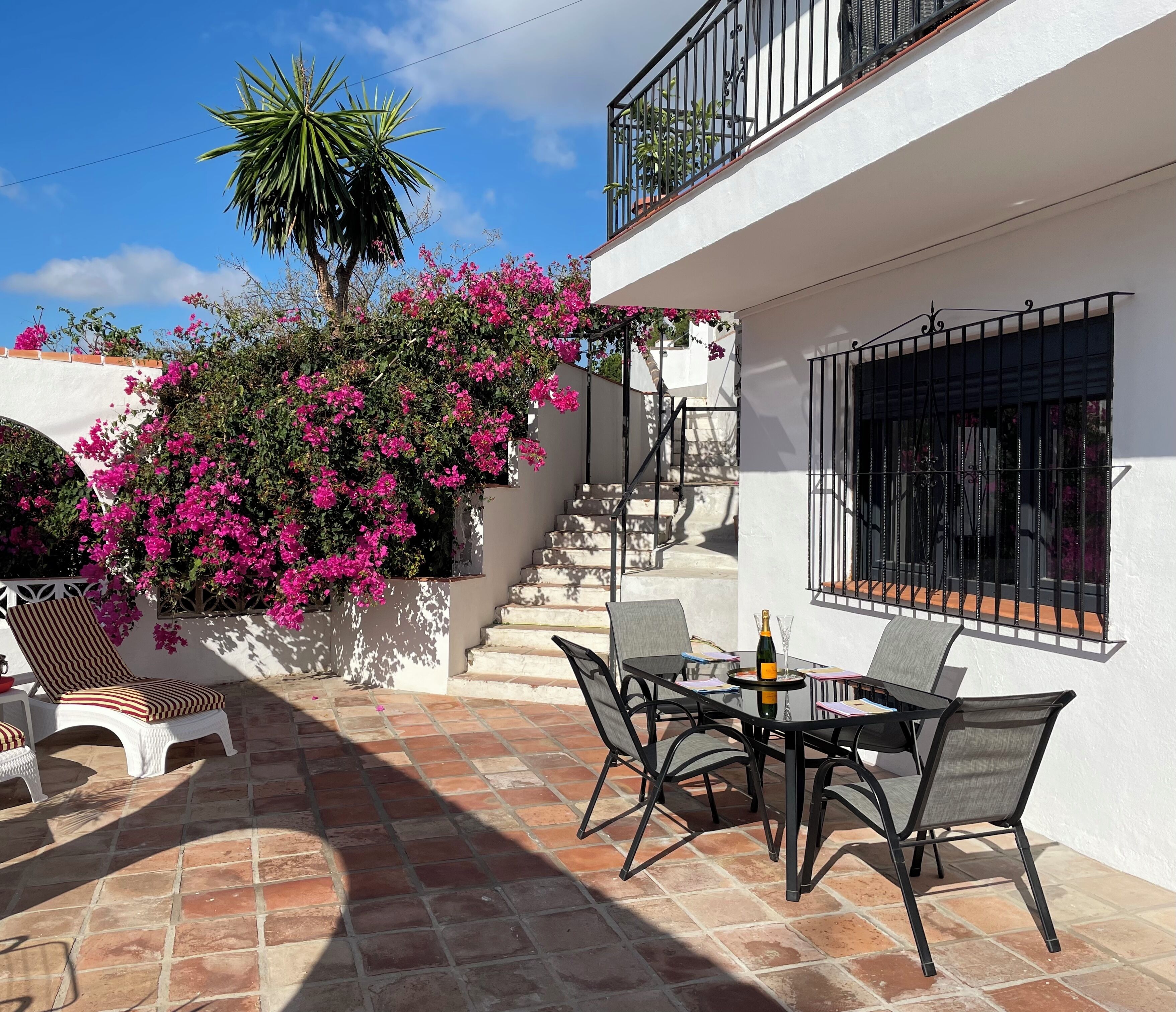 A patio with a table and chairs, a bottle of champagne, and a staircase leading to a balcony.
