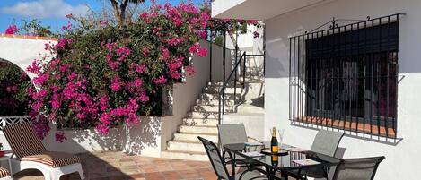 A patio with a table and chairs, a bottle of champagne, and a staircase leading to a balcony.