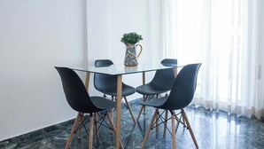 A glass table with four black chairs, a decorative pitcher with a plant, and a marble floor. - Modern 1 Bd Balcony Apt in Kato Patisia (Athens)