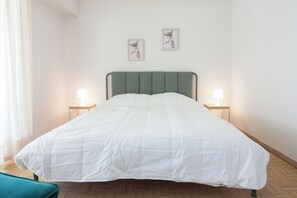 A neatly made bed with a green headboard, two bedside lamps, and two framed pictures on the wall. - Modern 1 Bd Balcony Apt in Kato Patisia (Athens)