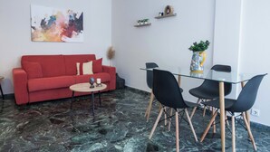 A modern living room with a red sofa, a glass dining table with black chairs, a marble floor, and a wall-mounted abstract painting. - Modern 1 Bd Balcony Apt in Kato Patisia (Athens)