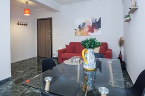A modern living room with a glass table, red sofa, and a painting on the wall. - Modern 1 Bd Balcony Apt in Kato Patisia (Athens)