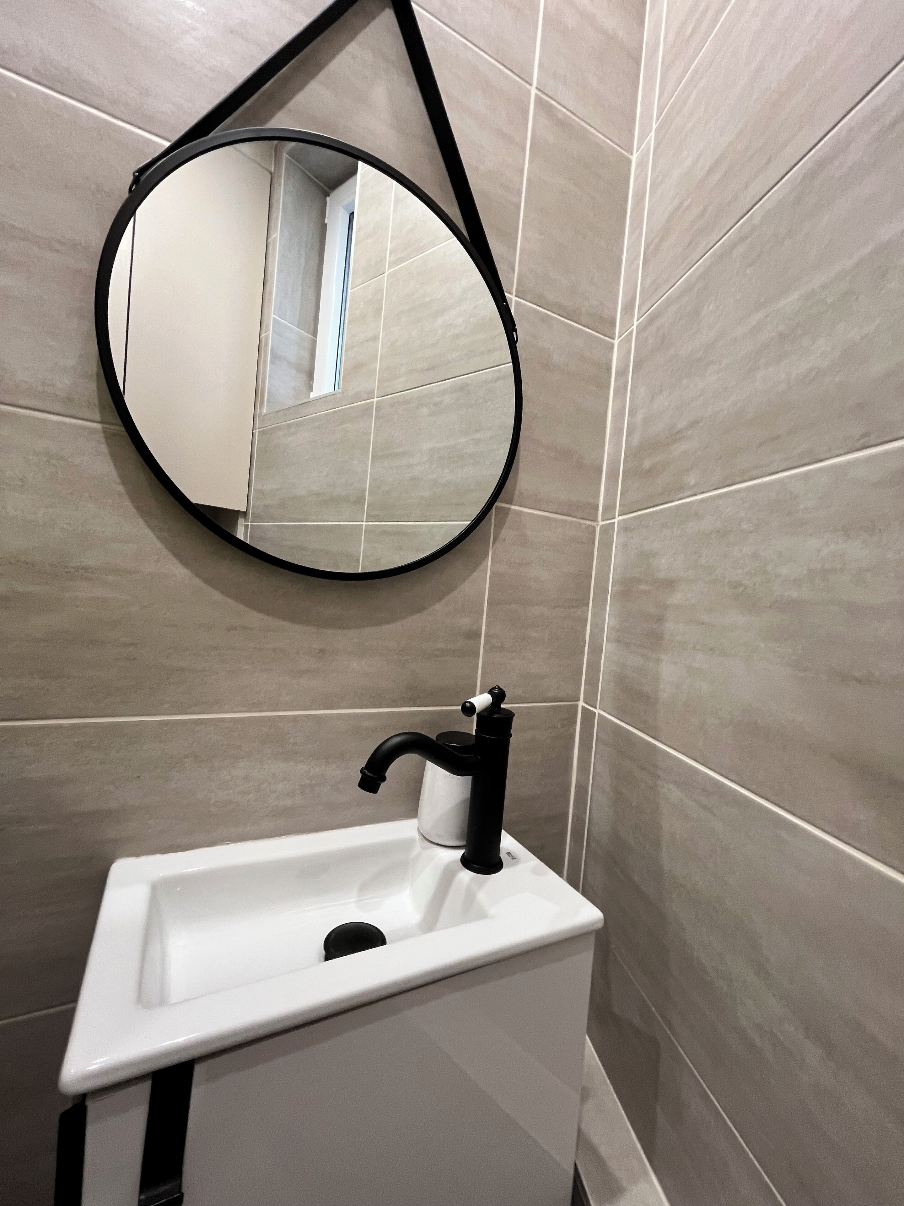 A bathroom with a white sink, a black faucet, and a round mirror on the wall.