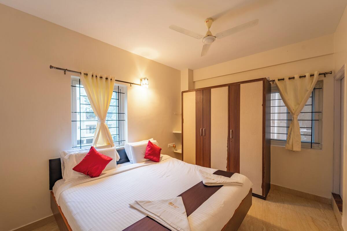 A hotel room with a bed, a wardrobe, a ceiling fan, and curtains.