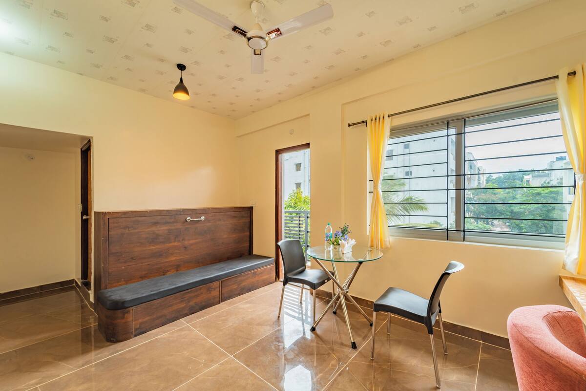 A room with a wooden bench, a glass table with chairs, a ceiling fan, and a window with curtains.