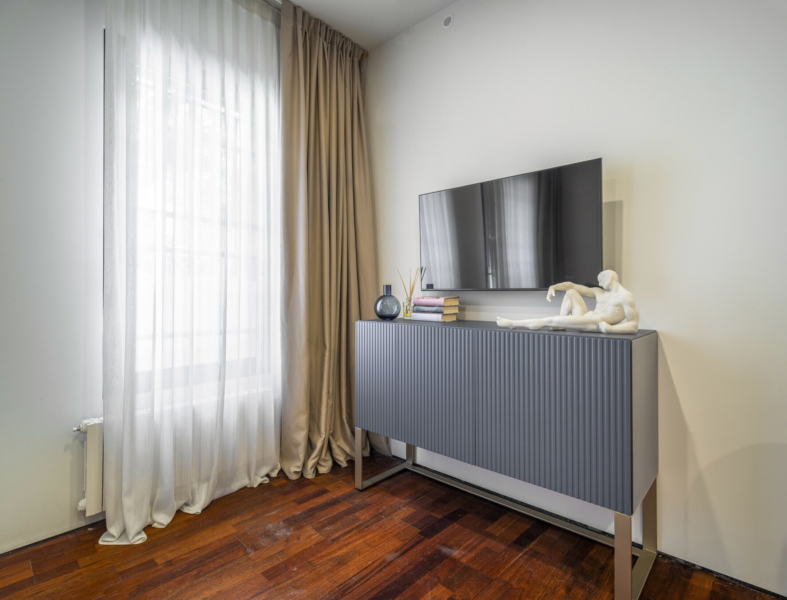 Una habitación moderna con una mesa consola gris, un televisor de pantalla plana y una escultura blanca.