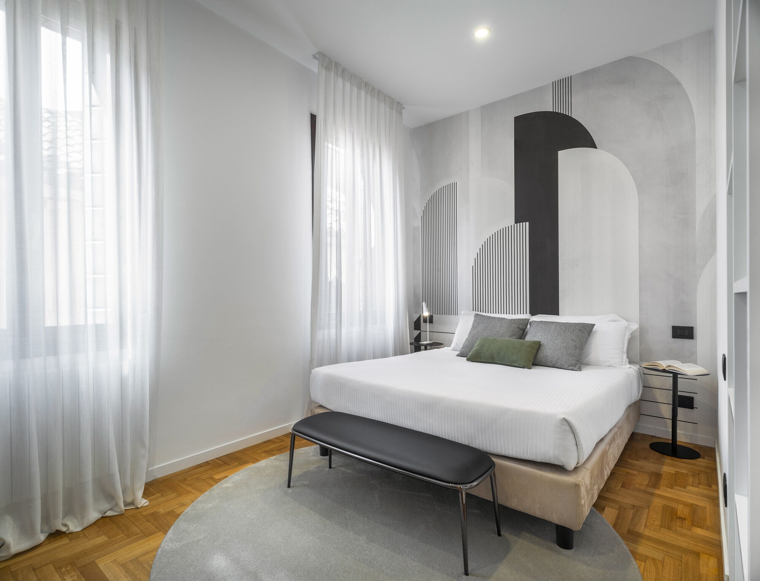 Un dormitorio moderno con una cama grande, un banco y una mesita de noche con lámpara.