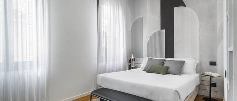 Un dormitorio moderno con una cama grande, un banco y una mesita de noche con lámpara.