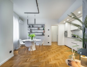 A modern kitchen with white cabinets, a built-in oven, and a herringbone wood floor.
