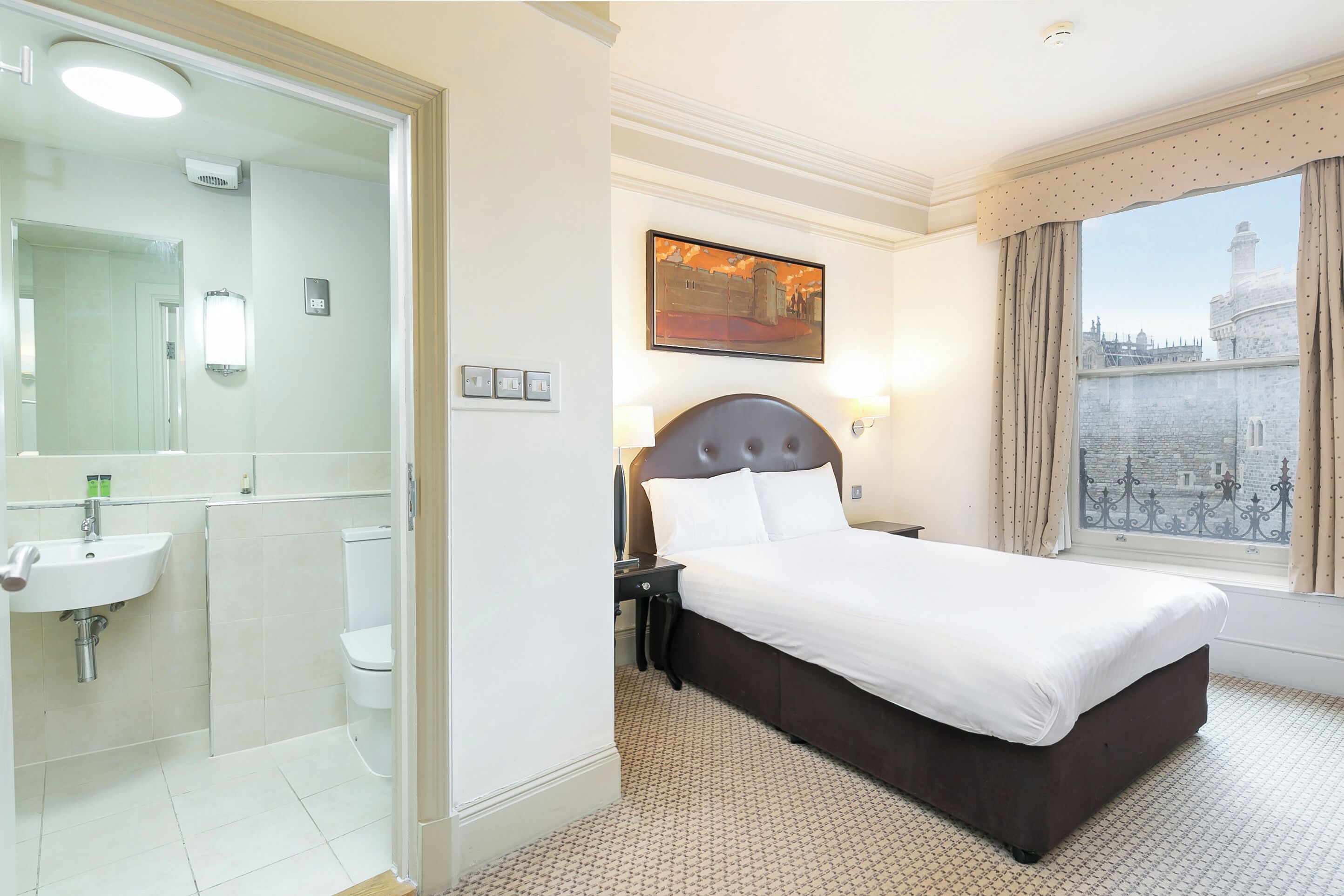 Hotelkamer met een groot bed, een badkamer met wastafel en toilet, en een raam met uitzicht op een gebouw.