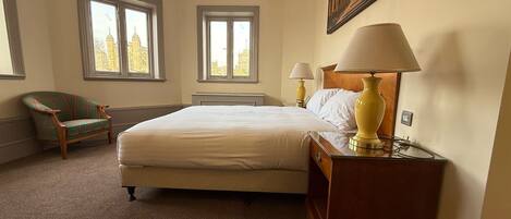 Habitación de hotel con una cama grande, dos lámparas de noche, una silla y dos ventanas con vista a la ciudad.