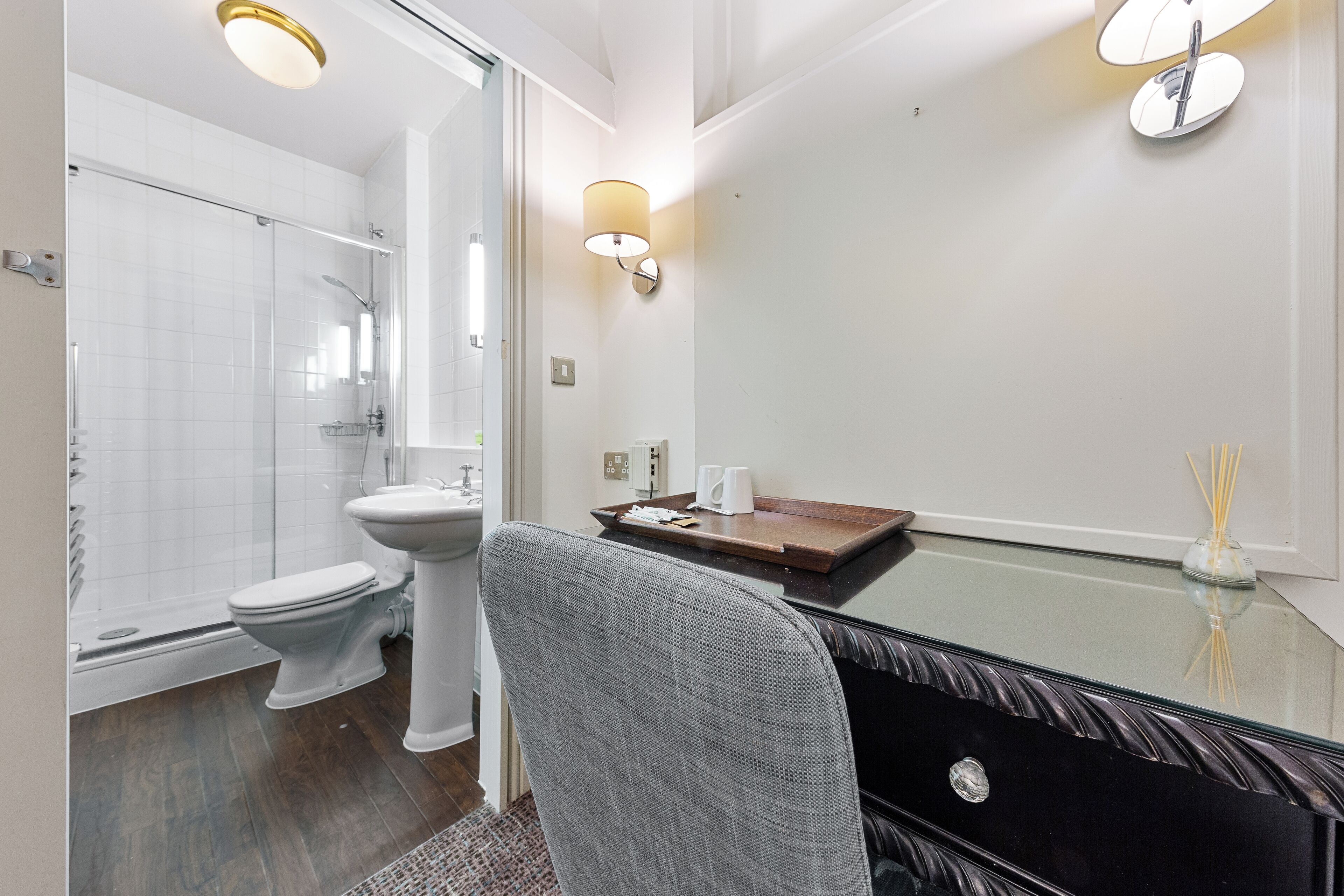A modern bathroom with a glass shower enclosure, a white pedestal sink, and a glass table with a chair.