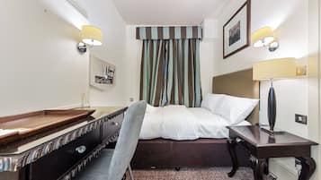 A hotel room with a bed, a desk, a chair, a lamp, and a picture on the wall.