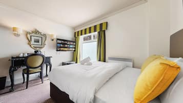 A hotel room with a large bed, a desk with a chair, a mirror, and a window with curtains.