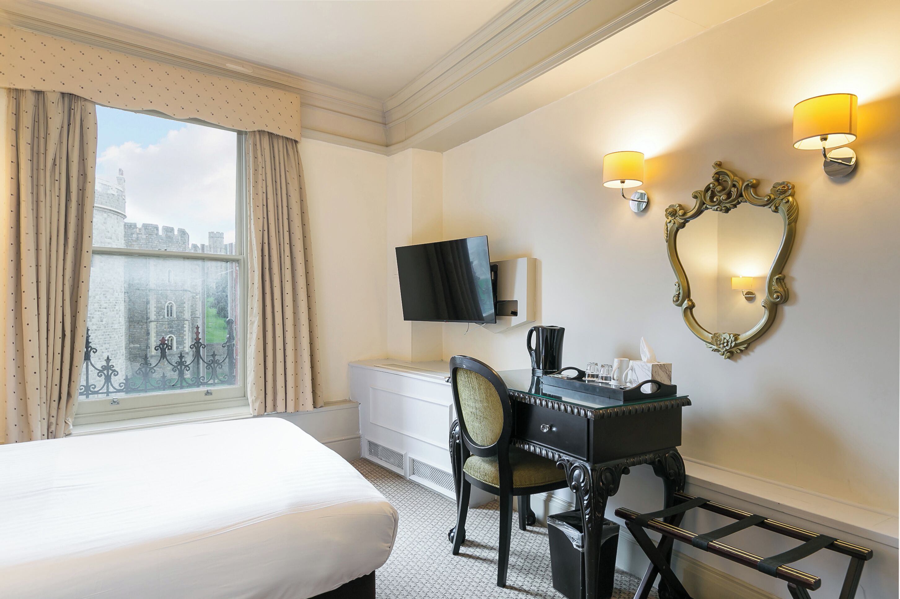 A hotel room with a bed, a desk with a chair, a television, a mirror, and a window with curtains.