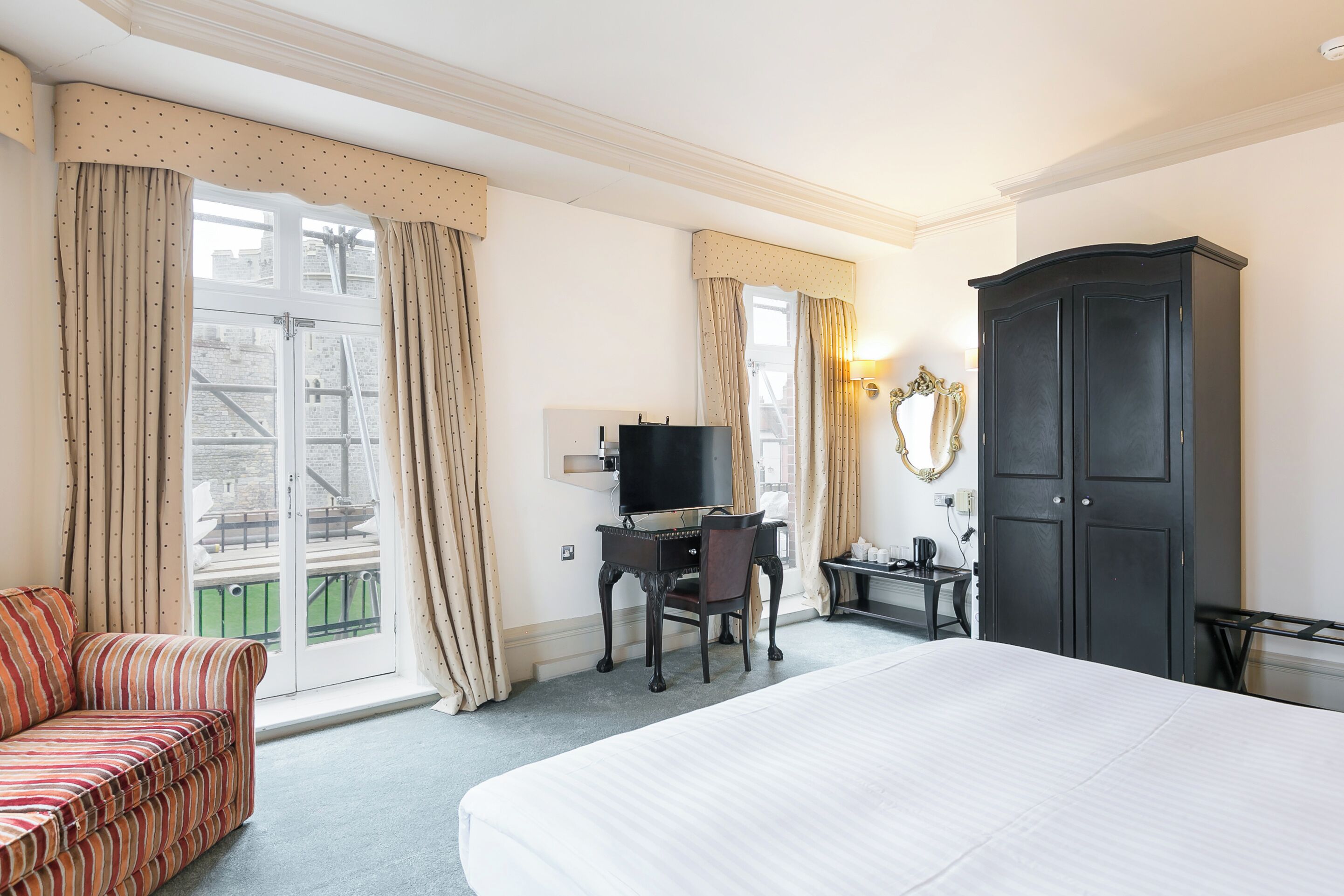 A hotel room with a bed, a desk with a computer, a chair, a wardrobe, and a sofa.