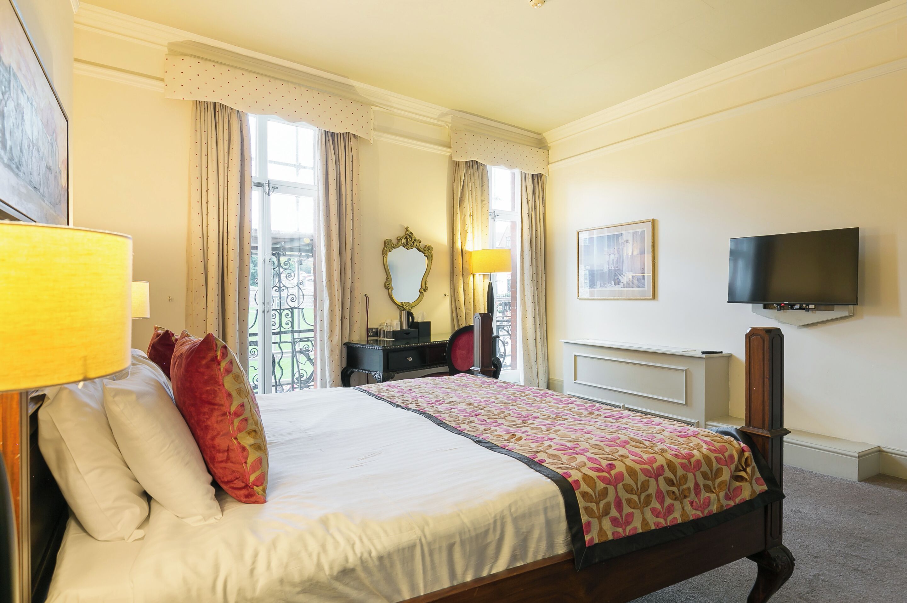 A hotel room with a bed, a TV, a desk, and a window with curtains.