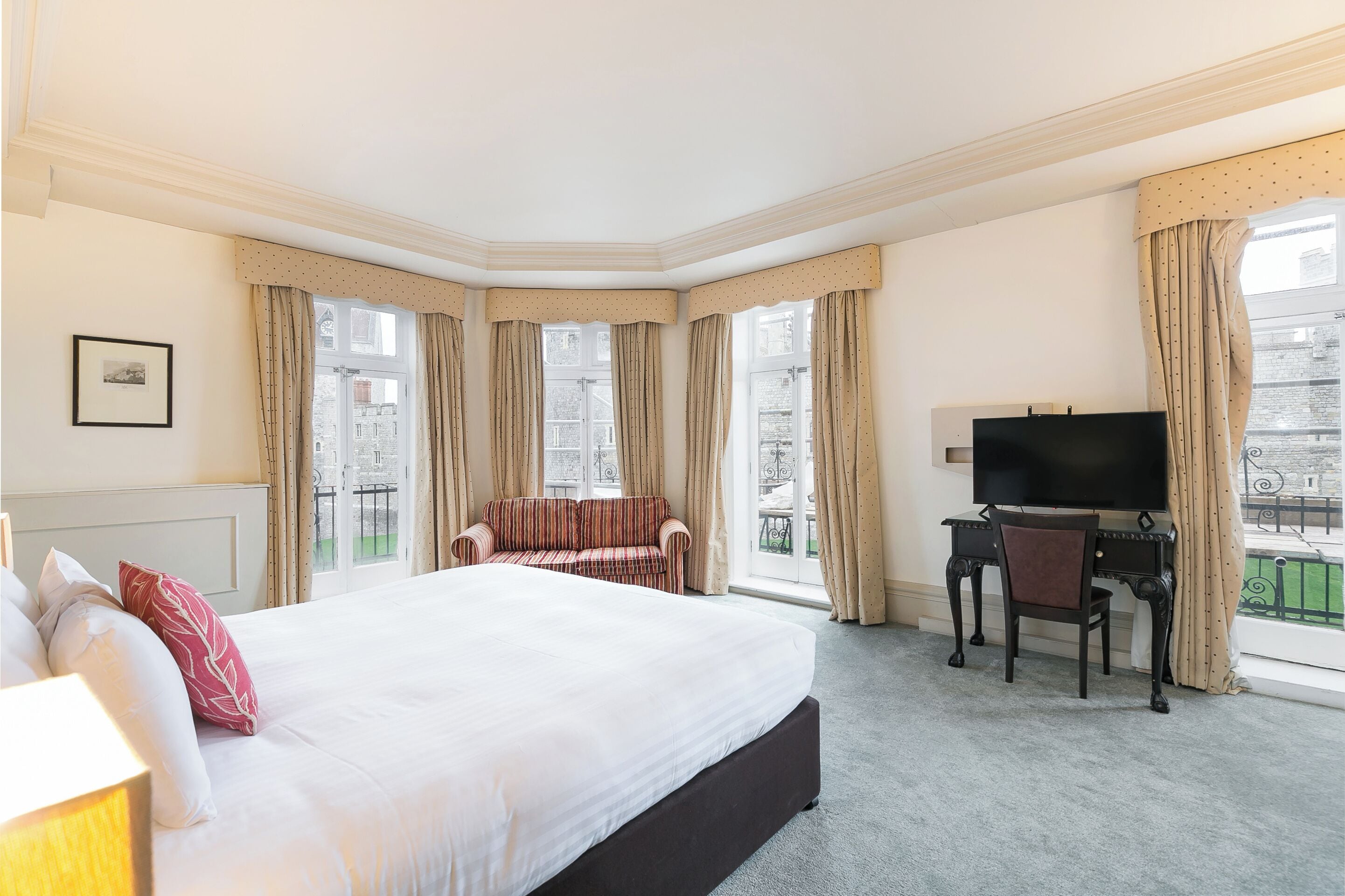 A hotel room with a large bed, a desk with a chair, a television, and a window with curtains.