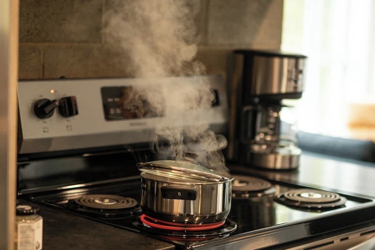 Uma panela de aço inoxidável sobre um fogão a gás com um anel vermelho, liberando vapor.