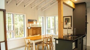 Una cocina moderna con ventanas amplias, una mesa de comedor de madera y una isla integrada.
