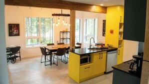 Una cocina moderna con una isla amarilla, encimeras negras y techo de madera. Amplias ventanas ofrecen luz natural y vistas al exterior.