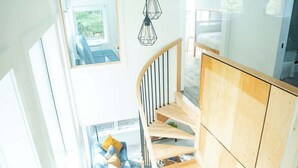 Un interior moderno con una escalera de madera, un sofá azul con cojines y vistas al exterior a través de una ventana.
