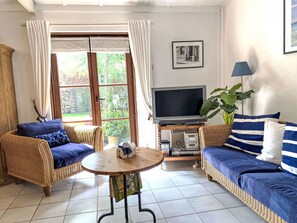 Ein Wohnzimmer mit Rattanmöbeln, einem Fernseher, einem Tisch und Blick durch eine Glastür.