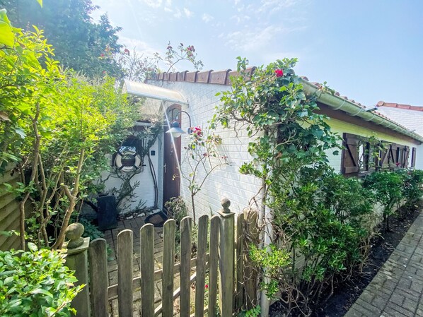 Un bâtiment blanc doté d’un toit incurvé, d’une clôture en bois et d’une végétation luxuriante.